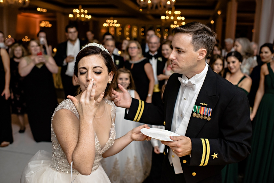 A wedding couple feed each other wedding cake in front of friend and family.